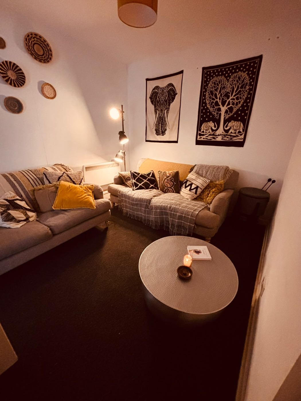 A cosy lounge with two sofas, cushions, throws and a candle on a round table.